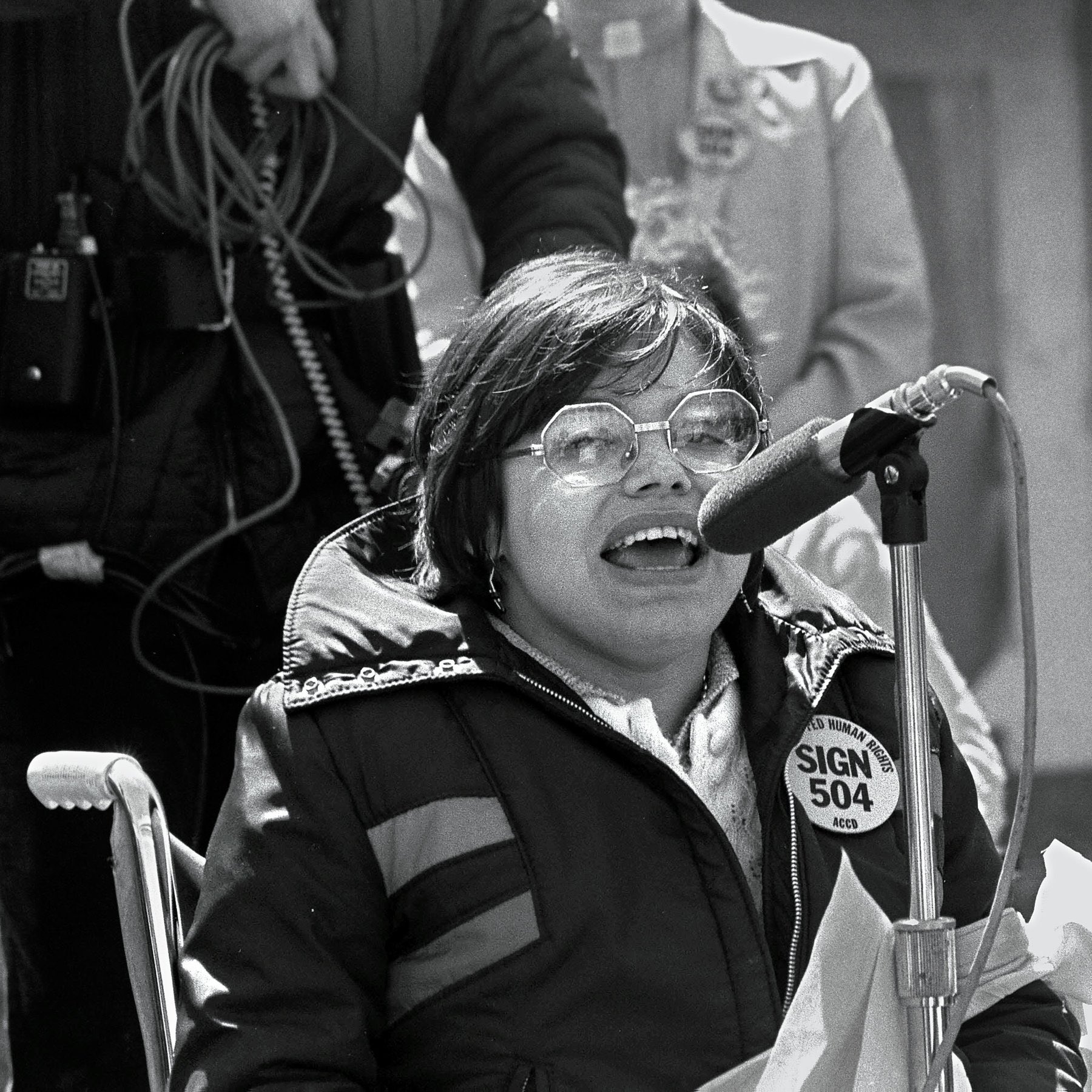 young Judy Heumann speaking into a microphone.