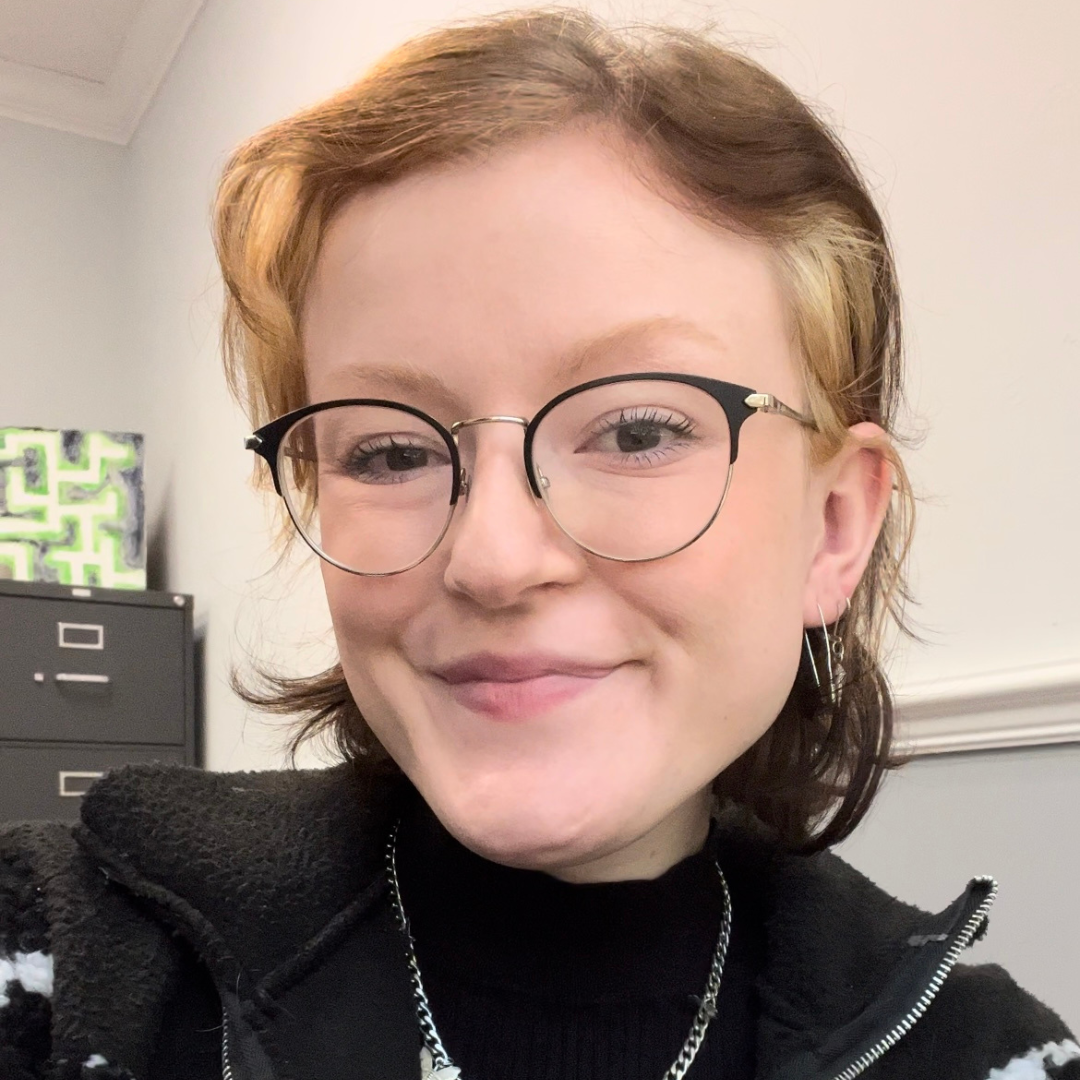 maddie, a white person white brown hair wears a black shirt, sweater and glasses