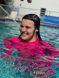 Ariana outside swimming in a pool. She has light skin, dark hair and wears a pink swimming outfit. She is smiling