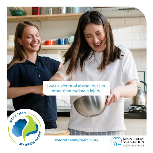 Image description: Photograph of two women in a kitchen smiling. The woman to the left is white with blonde hair and a blue shirt. The woman to the left is a white woman with brown hair wearing a white shirt and holding a silver bowl. Across the bottom there is a Brain Injury Association symbol with the phone number (1-800-444-6443) in blue and black text with a more than my brain injury hashtag and graphic of a person's side profile in front of a cloud.