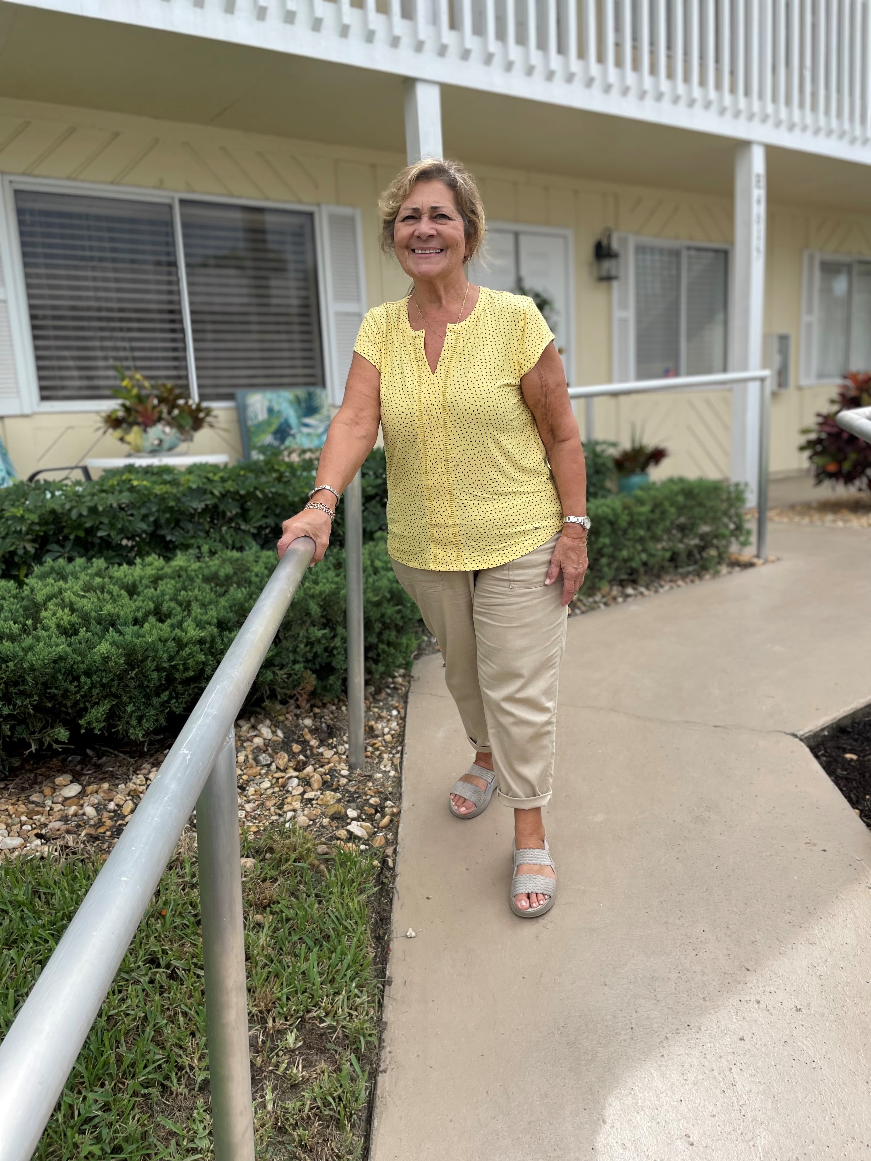 Client Carmina Vicidomini standing on a newly accessible path. She wears a yellow blouse and tan pants