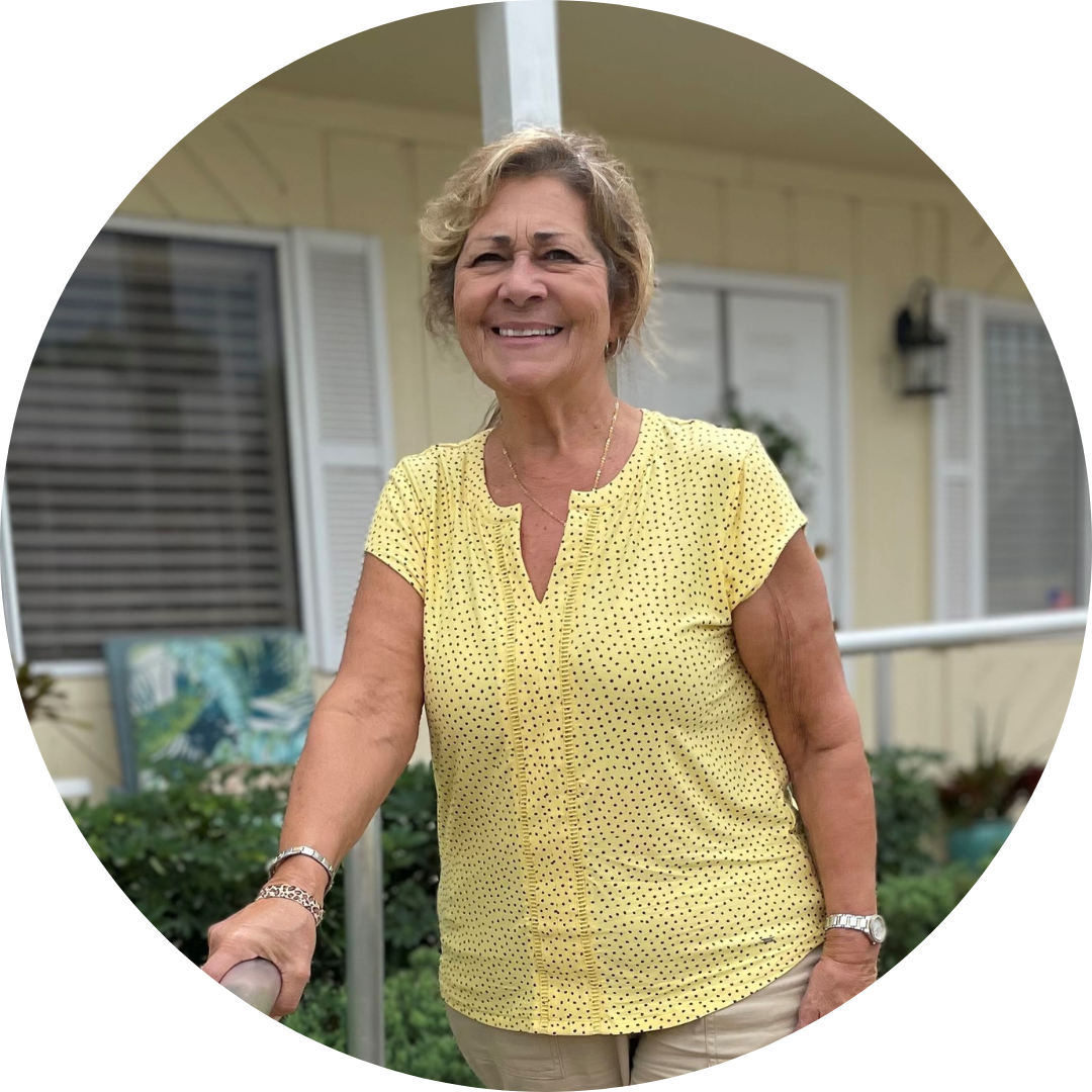 Carmina, a woman with lighter skin, standing on the new accessible pathway smiling. She wears a yellow shirt, khaki pants and sandals. 