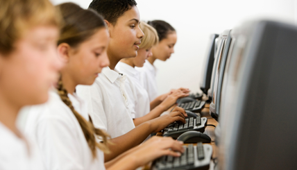 Students of various identities sitting in a computer lab, typing on desktop computers