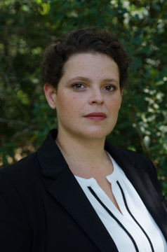 Caitlyn standing outside in front of trees. She has light skin, short brown hair, and wears a white shirt and black blazer