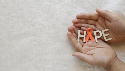 Beige fabric background with two hands that hold white letters spelling “Hope.” The “O” in hope is spelled using an orange ribbon. From Discovery Mood & Anxiety Program 