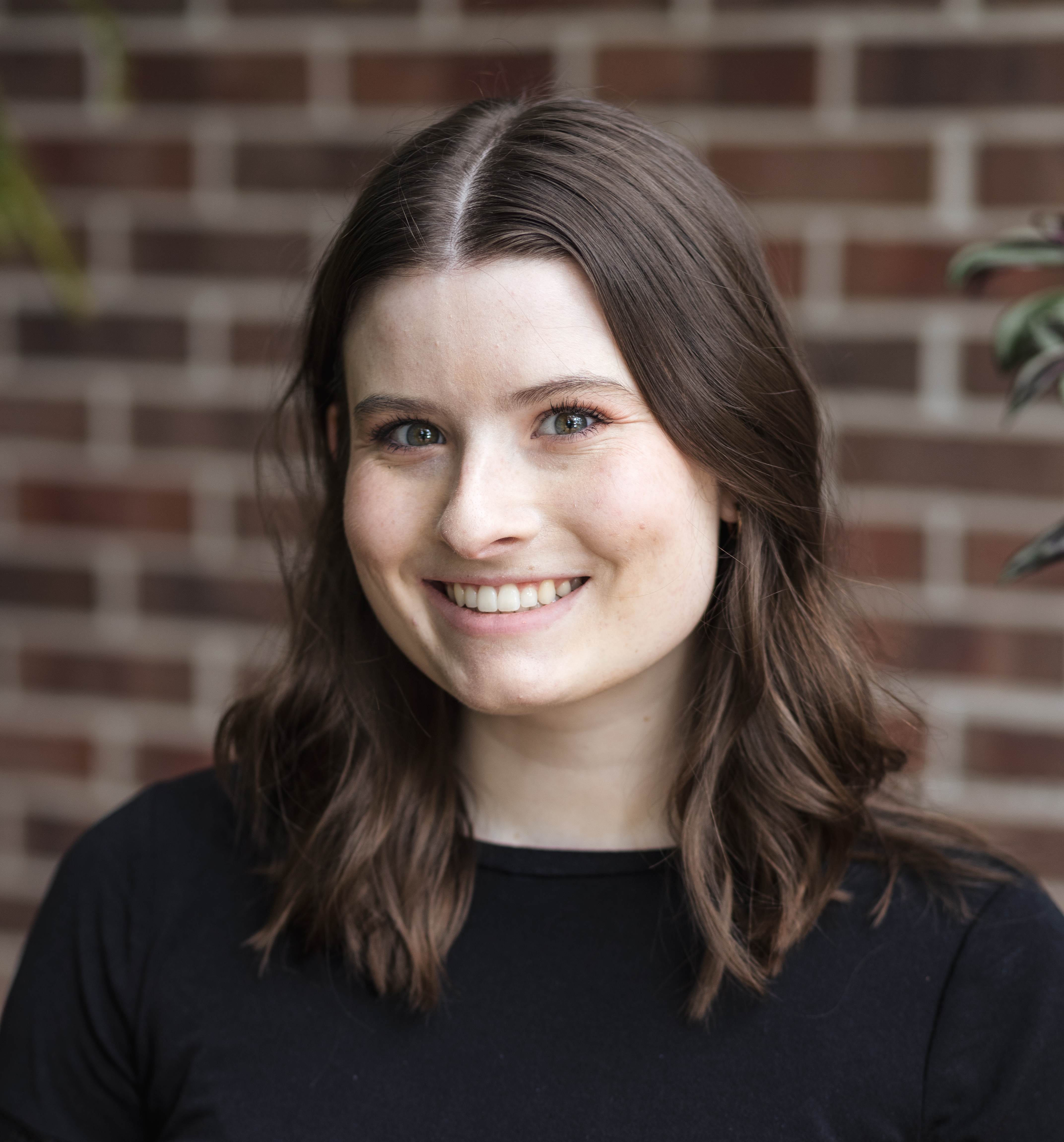 headshot of jamie butler, a woman with light skin, brown hair to her shoulders, wearing a black shirt standing in front of a brick wall