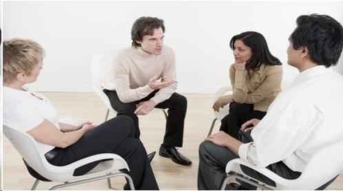 Photograph of four people in a talking in a group setting.