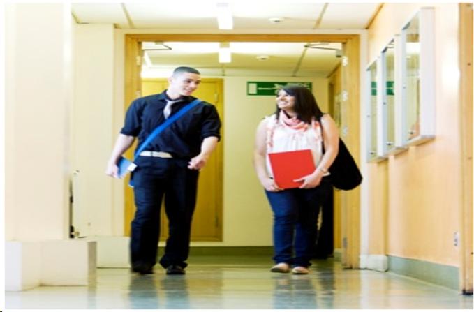 Photograph of two young people walking down a hallway, talking to each other.